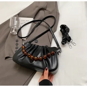 Detail van zwarte geplooide cloud bag met handvat van amber en leren schouderriem