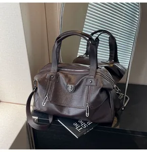 Detailed close-up of dark caramel brown leather tote with silver shield logo and twin zippers