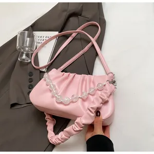 Detail van roze geplooide cloud bag met transparante kralenketting op witte stoffen achtergrond