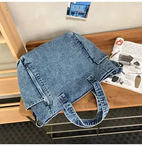 Detail of blue denim messenger bag with side pocket and sturdy handles on wooden desk