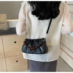 Detail van zwarte geplooide cloud bag met amberen kralenketting en leren schouderriem