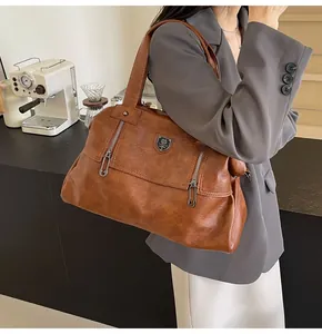 Detail of a large brown faux leather tote bag with unique pin-shaped zippers and shield emblem