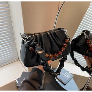 Detail van zwarte geplooide cloudtas met amberkleurige kralenketting en zilveren gespen