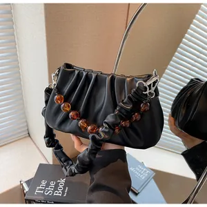 Detail van zwarte geplooide cloud-tas met amberkleurige kralenketting en zacht leer
