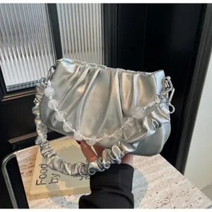 Detail van zilveren geplooide cloud bag met metallic finish en parelketting