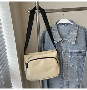 Détail du sac bandoulière en toile crème avec sangle noire et poche frontale zippée