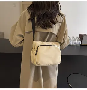Gros plan sur le sac bandoulière en nylon beige avec poche zippée et sangle noire