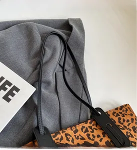 Detail of leopard print tote bag with black leather straps on grey suit background