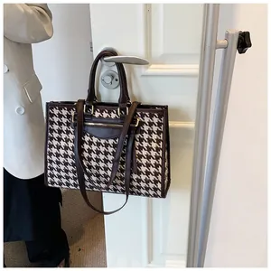 Detail of houndstooth tote bag with brown leather straps hanging on a door handle