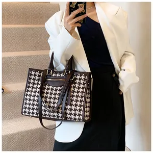 Houndstooth tote bag with brown leather handles worn by a model in a minimalist setting