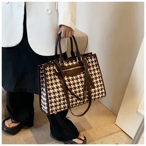 Detail of oversized houndstooth tote bag featuring premium brown leather straps and outer pocket