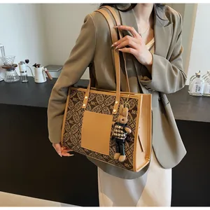 Close-up of brown tote bag with MC pattern and rabbit charm on a neutral background