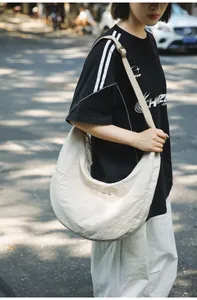 Outdoor street shot of large beige nylon hobo bag with wide strap and woven zipper pull