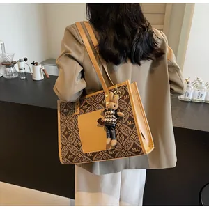 Chic monogram tote bag with leather trim and rabbit charm worn in cafe setting