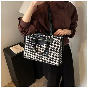 Detail of houndstooth pattern tote bag with leather handles and gold zipper accents