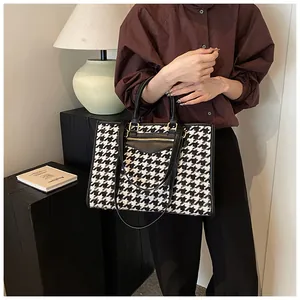 Close-up of houndstooth tote bag with black leather trim and golden zipper detail