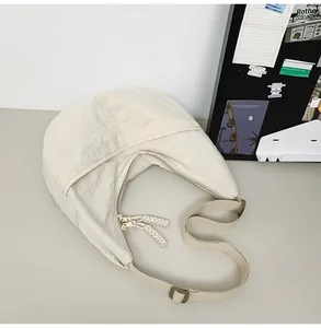 Detail of cream nylon crescent bag showing crinkled texture and braided zipper pull