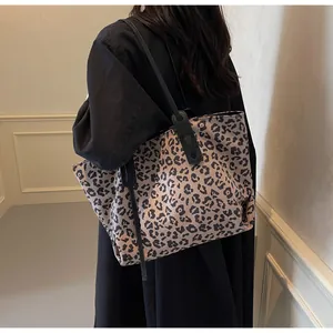 Detail of a leopard print tote bag featuring black leather straps on a winter coat outfit