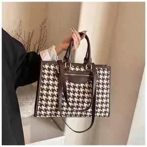 Detail of houndstooth tote bag featuring dark brown leather trim and golden metal zippers