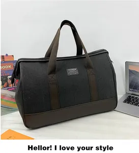 Large grey canvas travel bag with dark brown leather bottom in a lifestyle desk setting