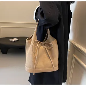 Detail view of beige matte suede bucket bag featuring a decorative bow tie and smooth leather trim