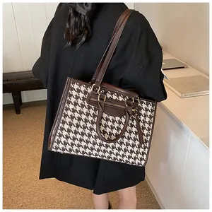 Classic houndstooth tote bag shown on shoulder with brown leather trim and golden hardware