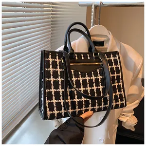 Detail of black and white plaid tote bag with faux leather trim and front zipper pocket