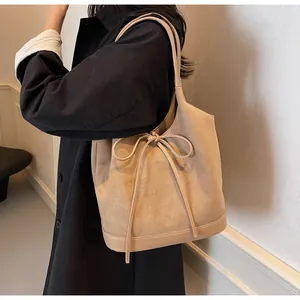 Detailed side view of beige matte suede tote bag with ribbon on black coat