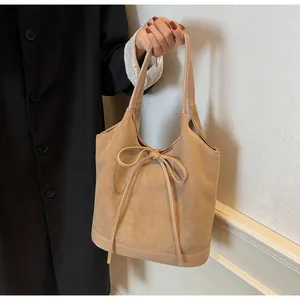 Close-up of beige suede tote bag featuring a bow tie design and smooth faux leather trim