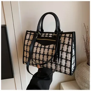 Close-up of black and white tweed tote bag with leather straps and gold zipper details