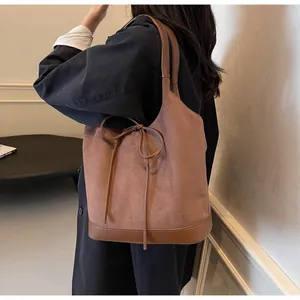 Brown suede bucket bag detail showing contrast stitching and bow decoration on the shoulder strap