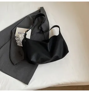 Gros plan du sac hobo noir à texture litchi avec boucle dorée sur un décor doux