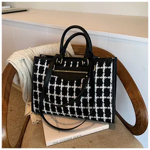Detail of black and white tweed tote bag with leather handles on a wooden chair