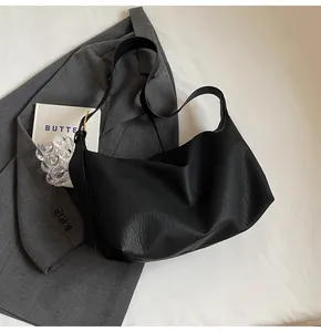 Gros plan du sac hobo en cuir noir à texture grainée sur un costume gris chic