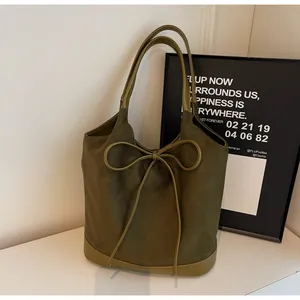 Detail of army green frosted bucket bag with leather bow and smooth trim on white table