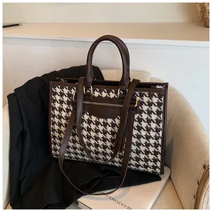 Detail of houndstooth tote bag with brown leather trim and metallic zipper accents