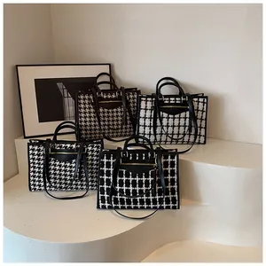 Detailed view of large tote bags with houndstooth patterns and leather handles on white steps