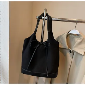 Detail of black suede tote bag with bow accent and leather trim hanging on a rack