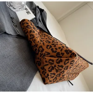Detail of leopard print tote bag with black straps on a grey suit blazer background