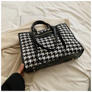 Macro detail of houndstooth tote bag with black leather accents and protective metal studs
