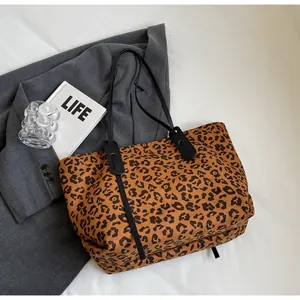 Detailed close-up of leopard print tote bag fabric and black leather shoulder straps