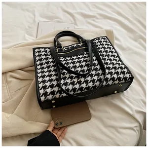 Detailed view of houndstooth tote bag with gold hardware and leather trim