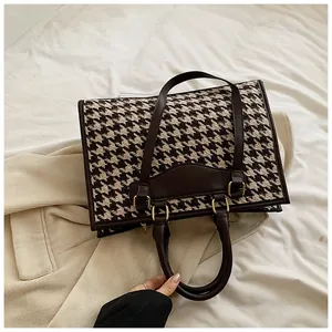 Detail of vintage houndstooth tote bag with brown leather handles and gold metal hardware