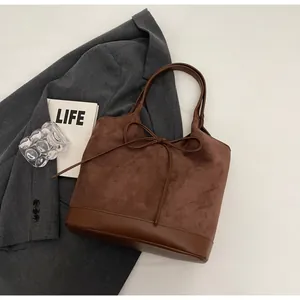 Detail of dark brown suede tote bag featuring leather bow knot and contrast textures