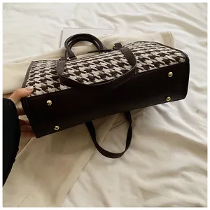 Detail view of houndstooth tote bag bottom with protective gold metal feet and brown trim