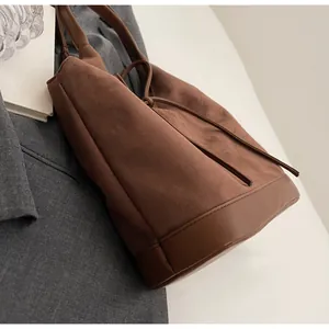 Detailed close-up of dark brown suede tote bag with textured leather stitching and bow drawstring