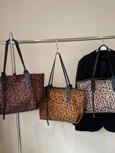 Three oversized leopard print tote bags in different shades hanging on a minimal rack