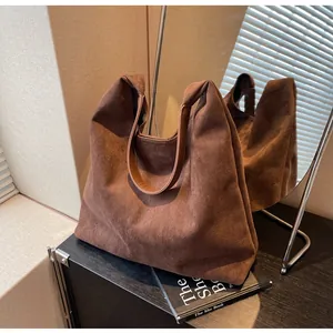 Detail view of a large brown suede hobo tote bag with premium leather straps on a desk