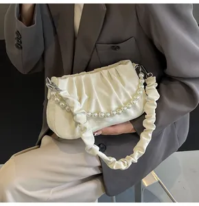 Close-up of pleated cream shoulder bag with pearl strap and silk-like textured fabric