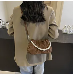Detailed view of brown ruched crossbody bag featuring an elegant pearl chain strap